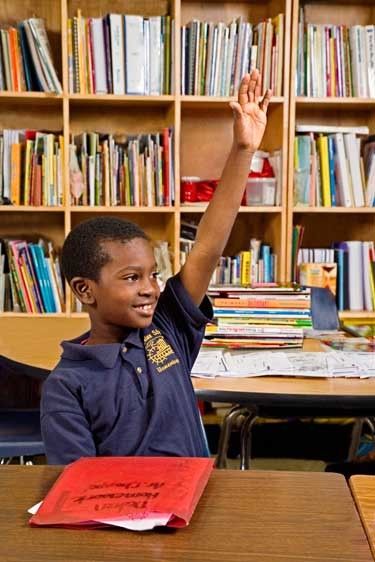 Black smiling second grade boy sits at desk and raises his hand in class in Louisiana school African American boy raises hand in classroom