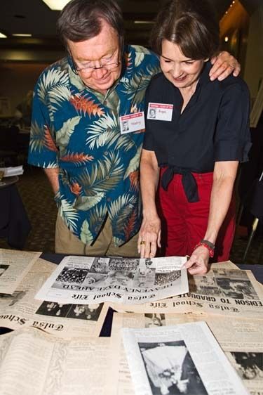 Two adult seniors reminisce about high school and look at school newspapers at class reunion Two seniors- Man and Woman- look at newspaper clippings at reunion