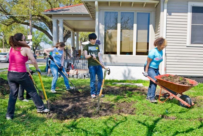 Young women and young man students dig with shovels and haul wheelbarrow in yard of New Orleans home in the 9th ward Teen college students volunteer outdoors in New Orleans