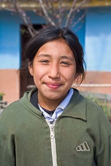 Young girl, nine years old, smiles in front of school in Peru One Peruvian school girl stands outside of classroom_ portrait