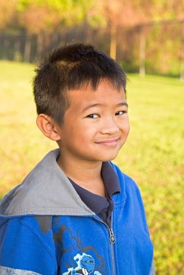 One second grade Vietnamese American boy poses on school ground for portrait outdoors Seven year old Vietnamese boy headshot on schoolground outdoors