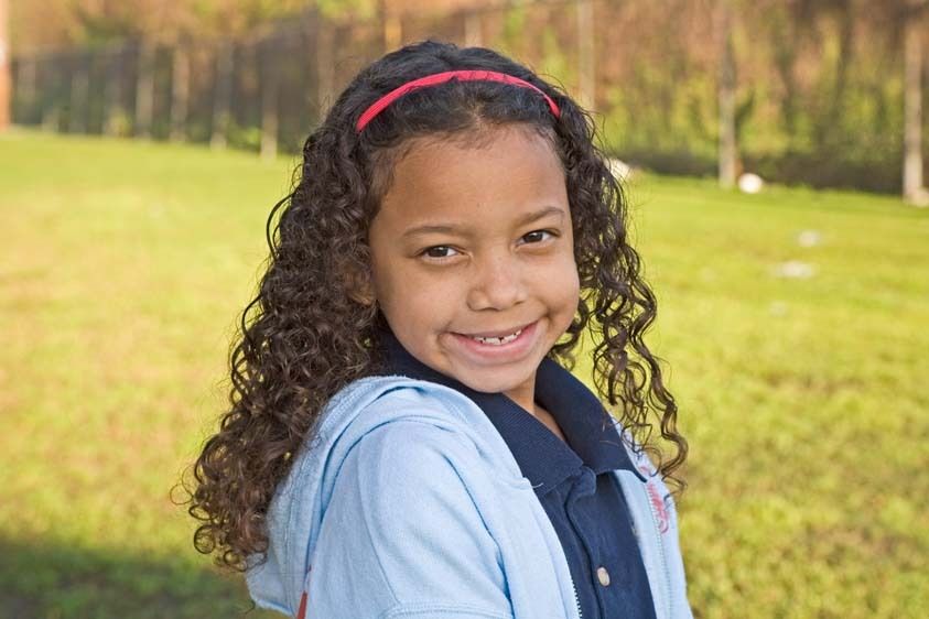 Happy seven year old mixed race of African American descent female child headshot outdoorsin New Orleans, Louisiana Curly headed mix race seven year old girl portrait