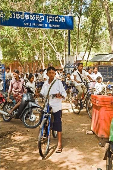 Children leave Cambodian school through gate on bicycles and motorcycles in Siem Reap, Cambodia Cambodia students leave school on bicycles and motorcycles