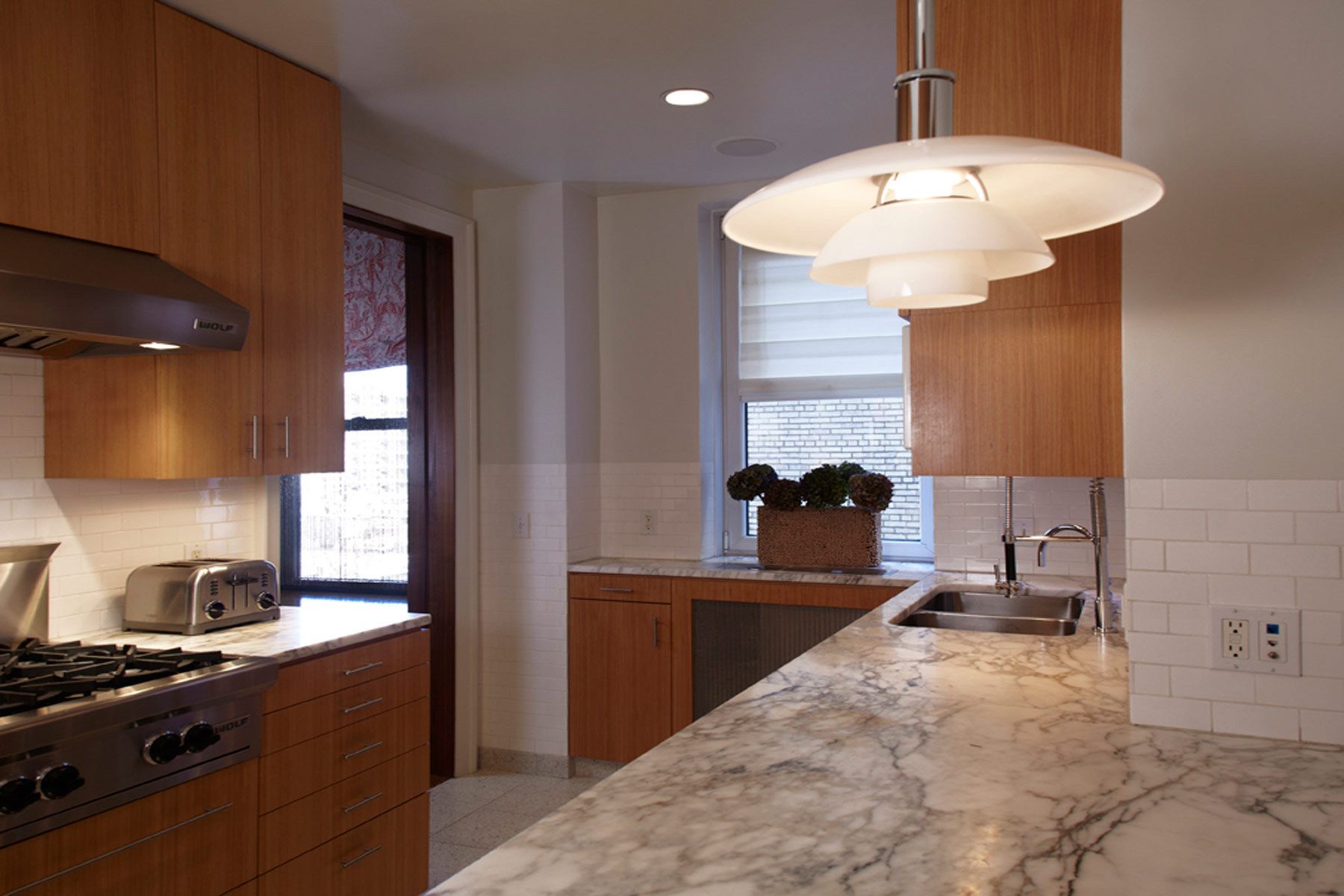 This apartment renovation features rich nut-wood veneers, walnut for the doors and pecan for the kitchen cabinetry, complemented with outsized patterned wallpaper in the entry vestibule and den.  The gallery is furnished with a Serge Mouille chandelier casting light on the silver leafed ceiling, a bronze wall-mounted BDDW vacuum tube clock, and a shagreen-fronted Roman Thomas console.Construction was completed in 2006, and Belsey & Mahla Architects continues to provide design services to the owners. West 86th Street