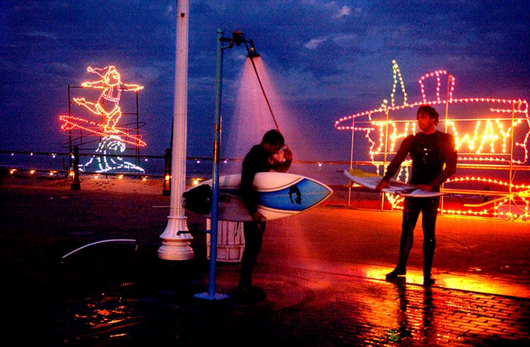 The holiday lights of the Virginia Beach boardwalk gleam behind locals Billy Goodson, left, and John Malbon as they rinse off after a day of surfing at the First Street jetty in Virginia Beach. Malbon said he enjoys the surfing spot this time of year when there aren't as many tourists. 1surfphotoportfolio_copy