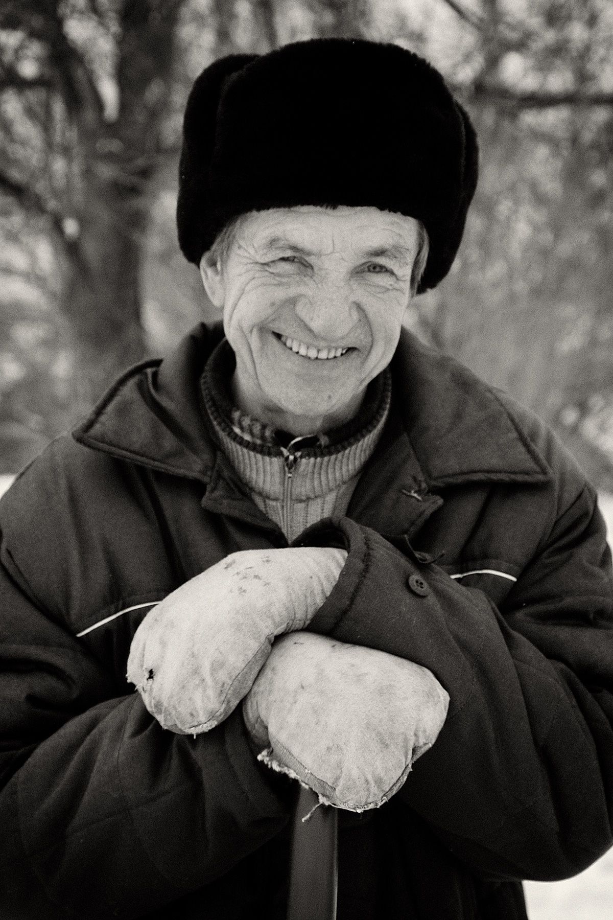 Russian man with ushanka and mittens shoveling snow in a Russian village. Russian Man in Village