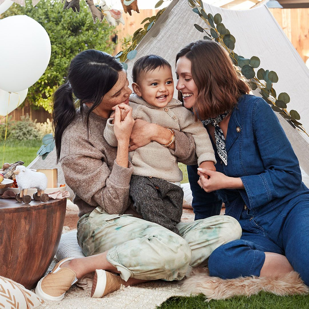 two moms smiling while holding baby at a birthday party two moms holding baby at a birthday party