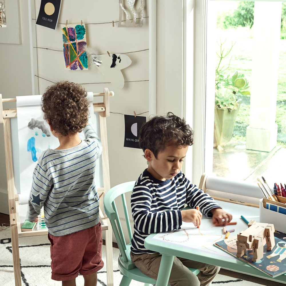 one little boy paints on an esile while another draws on paper at a table with crayons. photo retouching by jon birdseye two little boys creating art