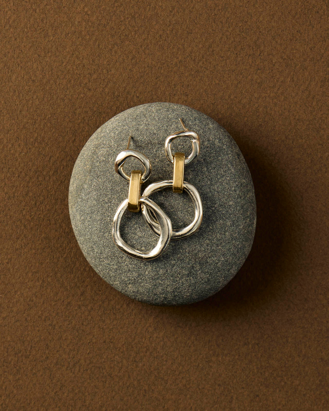 silver and gold earrings sit on a textured grey rock 