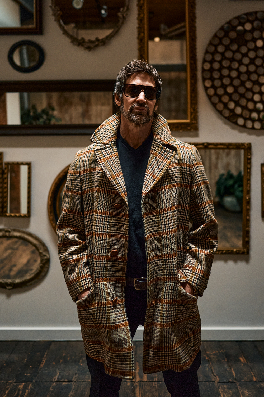man poses in checkered coat standing in front of gallery wall Saints And Savages