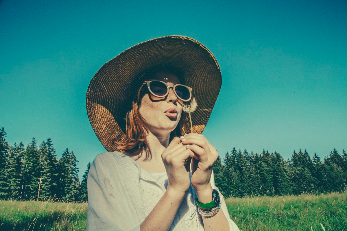 Woman In Hat Blowing On Dandelion By Seattle Lifestyle Photographer Alison Blomgren.