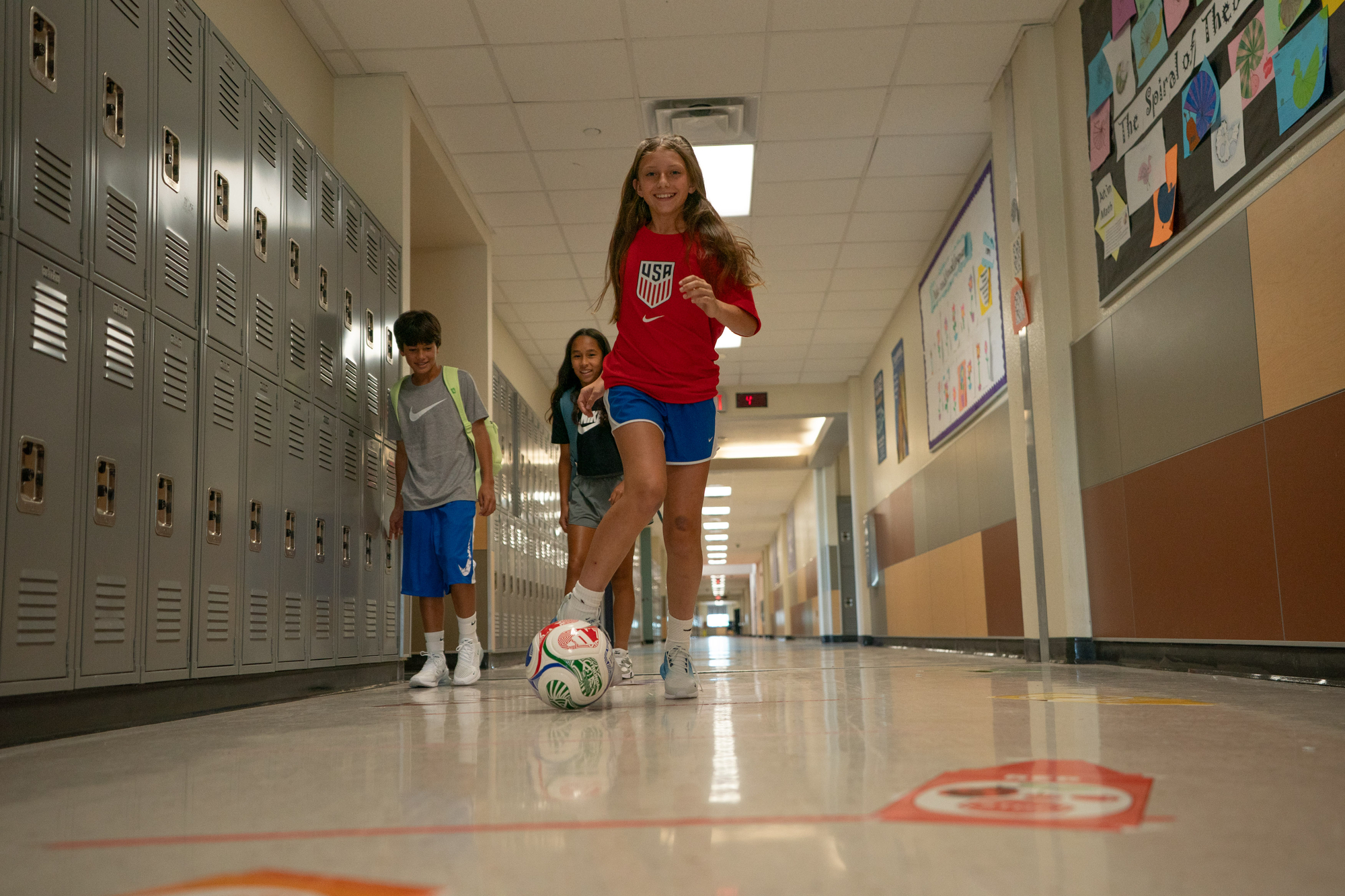 young girl kicks soccer ball in school halls 