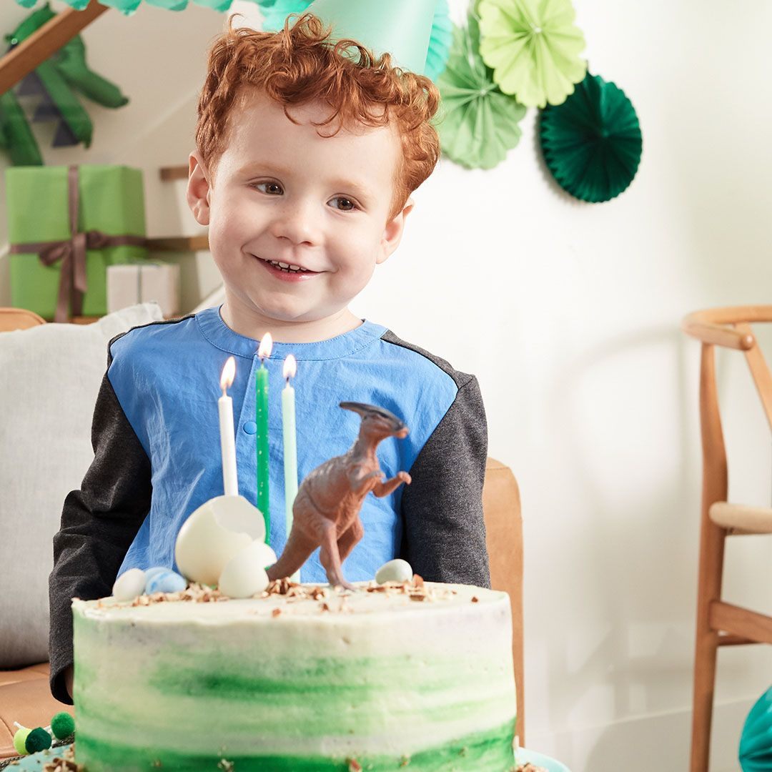 red headed little boy poses in front of a dinosaur theme birthday cake