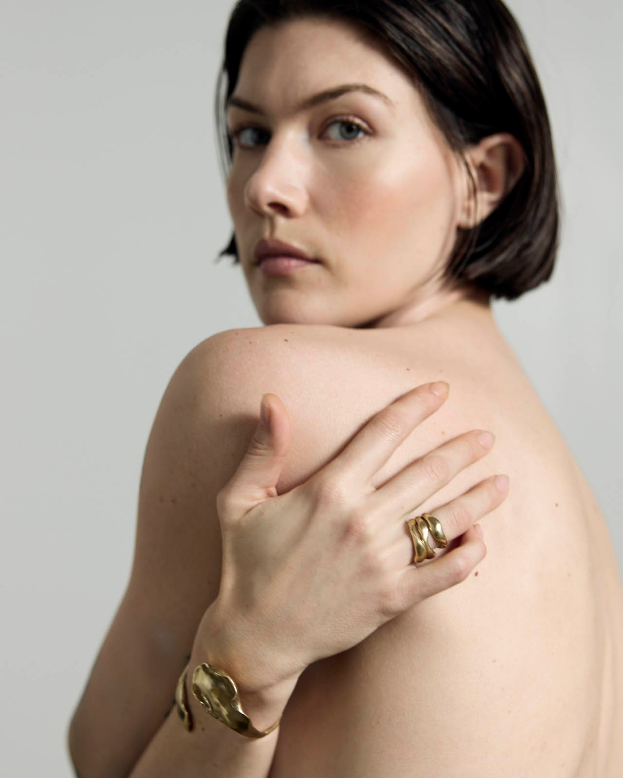 woman with brown bob looks over her shoulder adorned in golden jewelry 