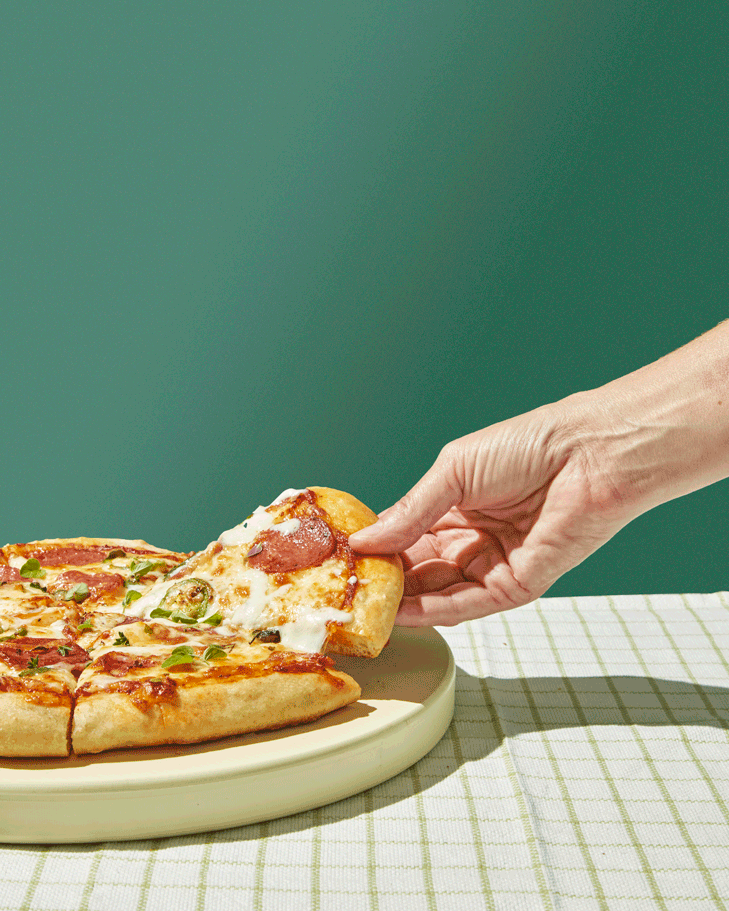 Gooey pizza slice is pulled off the circular stone platter on the green checkered tablecloth. Delicious supreme pie