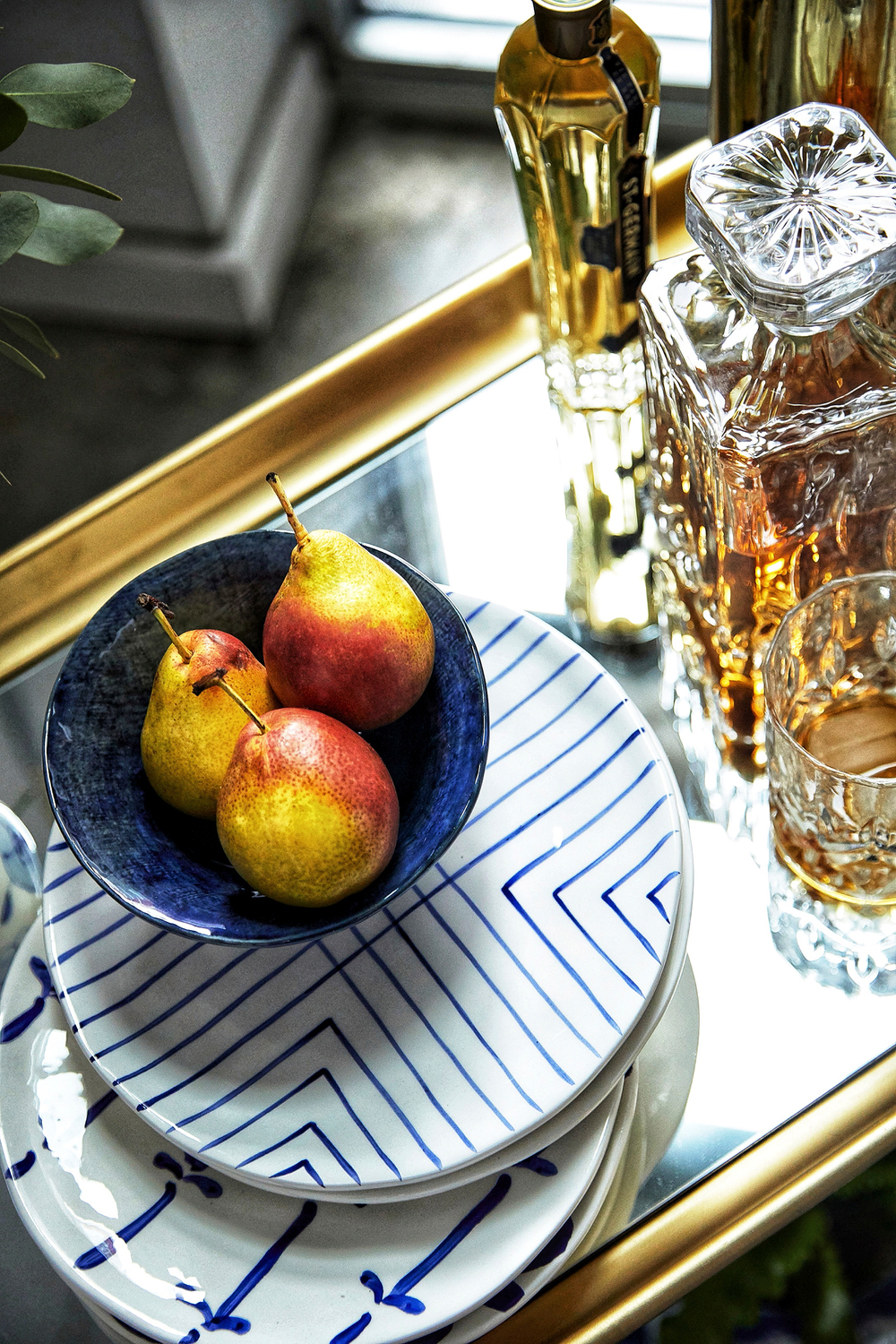 Beautiful decorative tabletop ideas for parties, vintage crystal whiskey decanter, st Germain elderflower liqueur, organic fruit display, white plates with a blue design Reflective surface on the cocktail cart