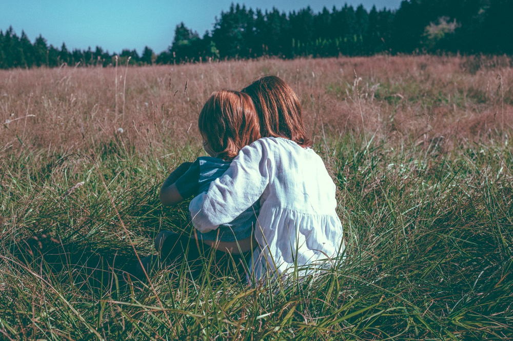 two siblings sitting together in a field