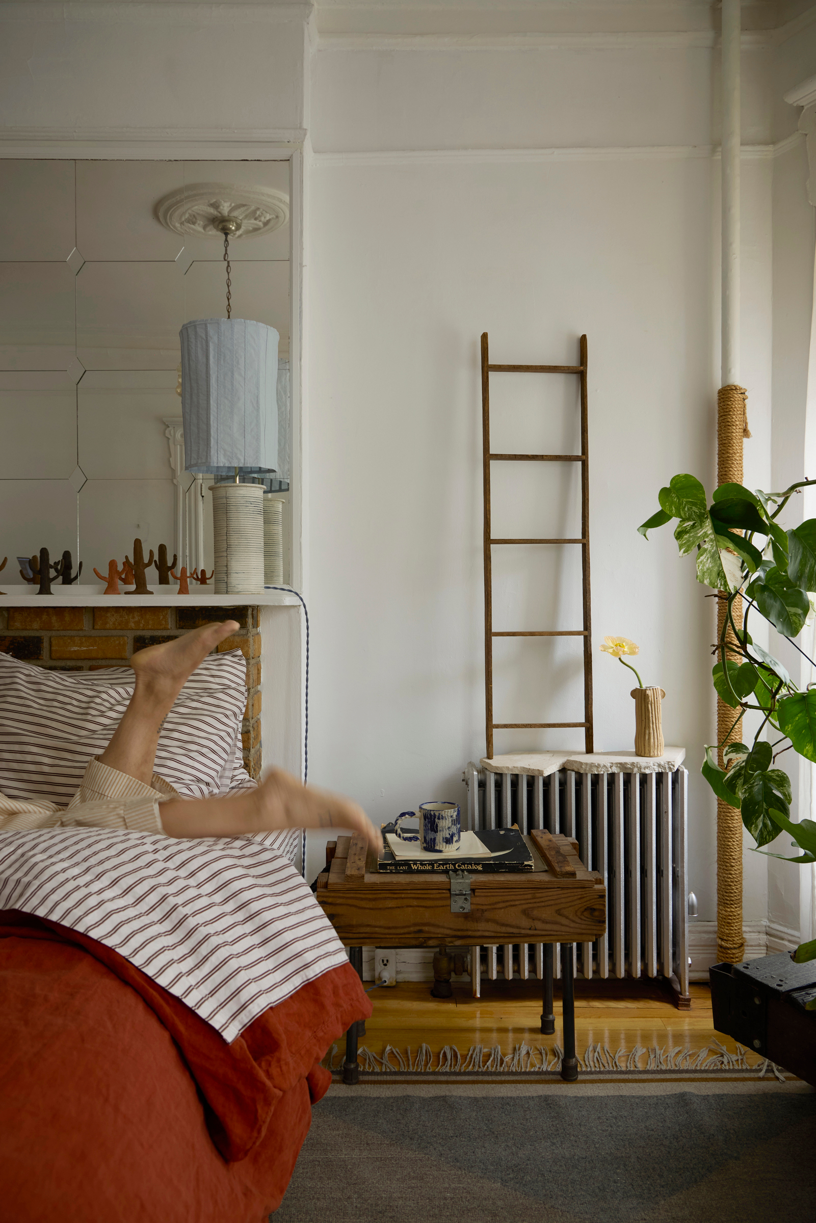 brooklyn loft bedroom with striped comforter and wooden nightstand, radiator and fresh plants photographed by George Barberis Interiors By George Barberis