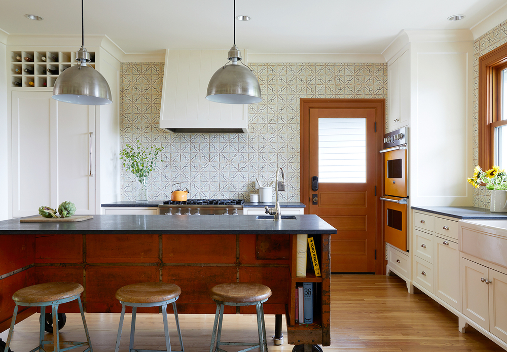 Rounded metal light fixture, exposed wood trim, tiled wall, unique orange oven with stainless steel, orange tea kettle, warm hues Home kitchen with sunflowers