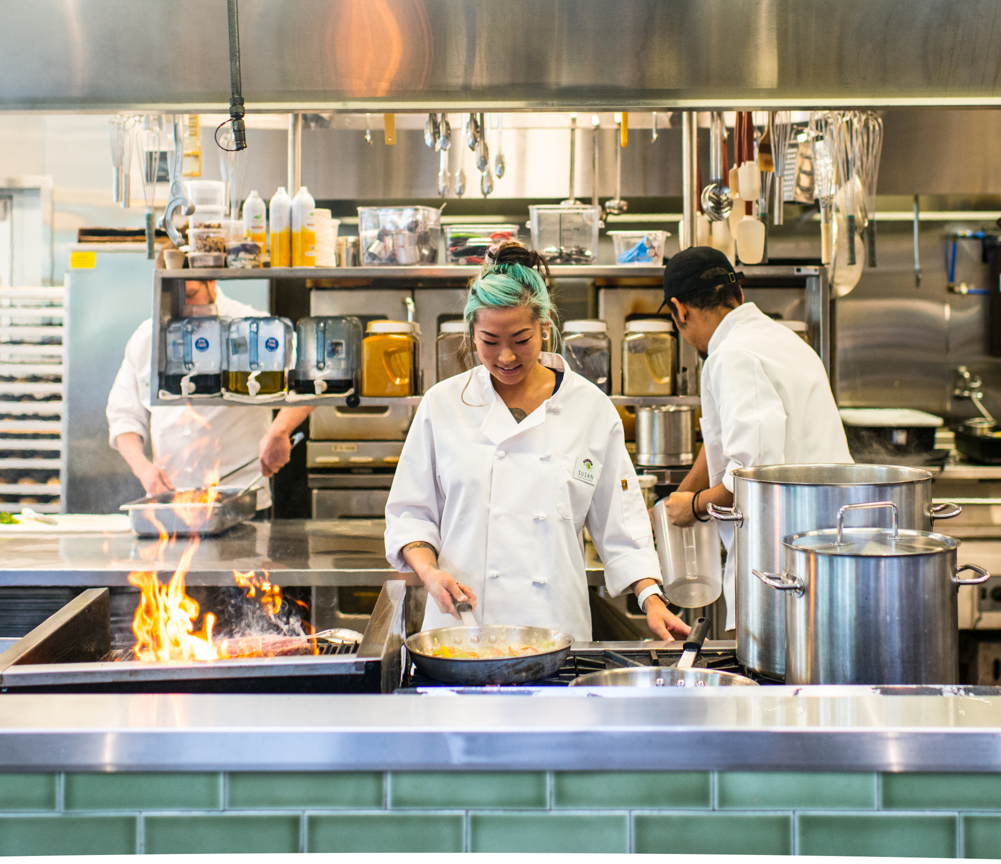 Watching through the window framed by green tiles as three people keep busy in the kitchen Smiling cook with wild hair