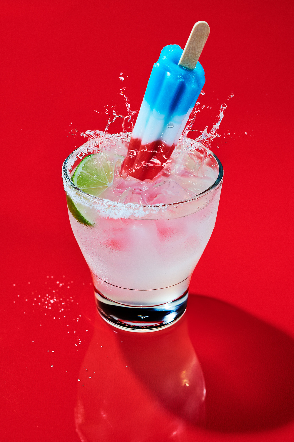 Festive summer cocktail on a glossy red background. Margarita with popcicle garnish