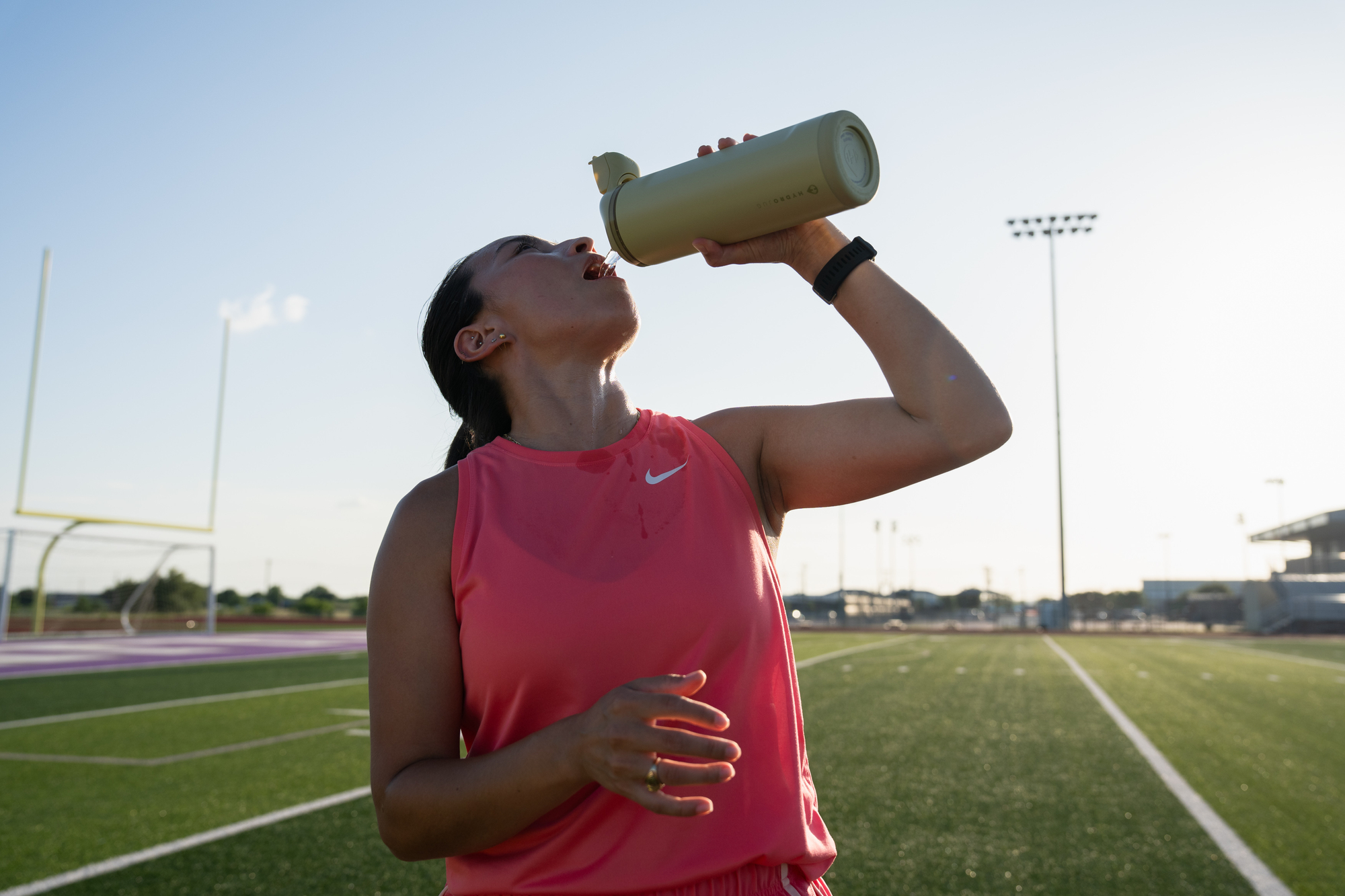 female runner chugs water on the track field 