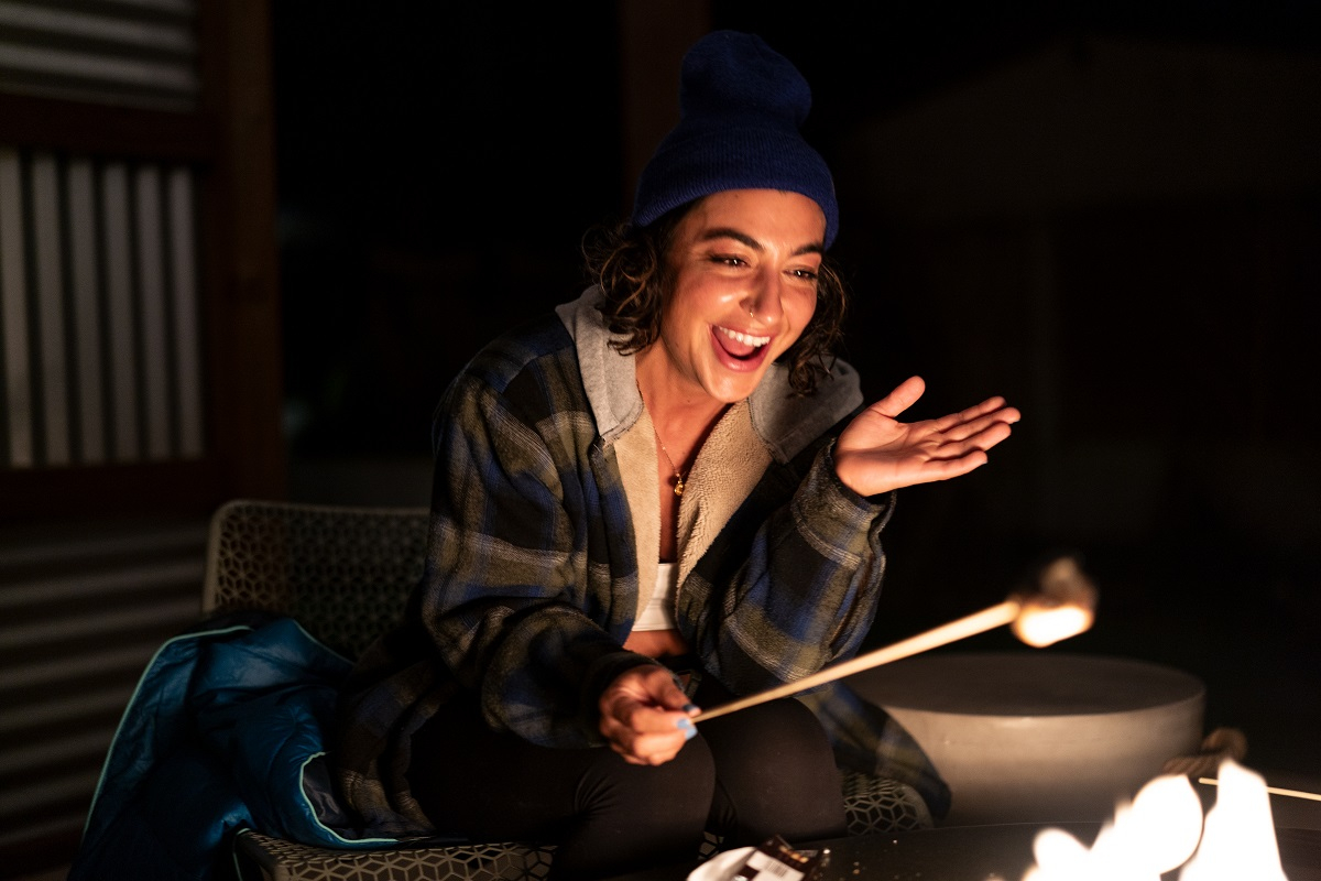 young woman in blue beanie roasts smores over the fire 