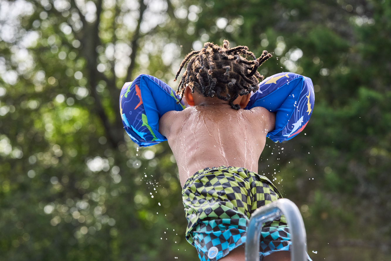young boy jumps into pool with arm floaties 