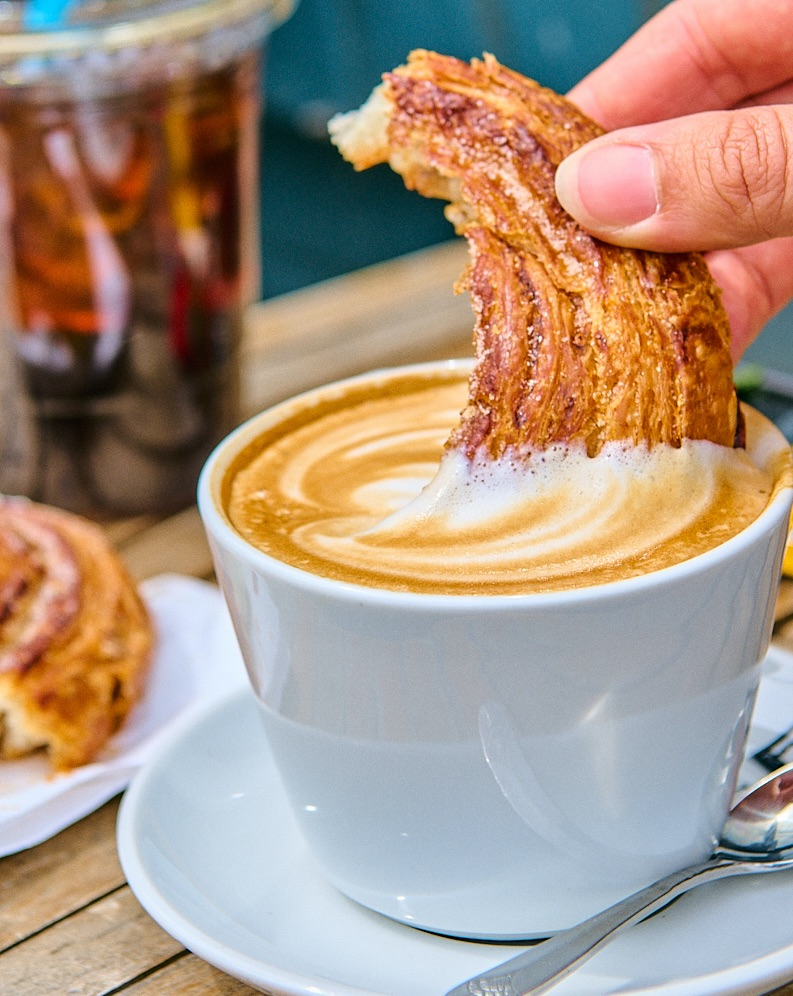 woman dips raisin roll into latte 