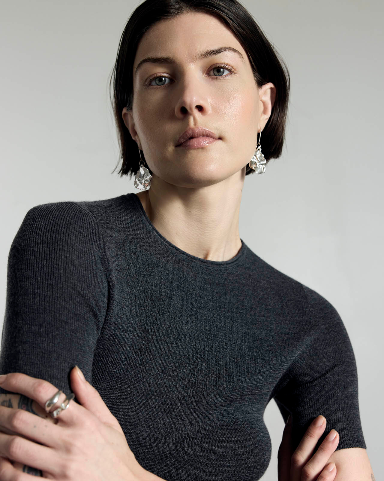 woman with brown bob and blue eyes poses in grey long sleeve with silver jewelry 