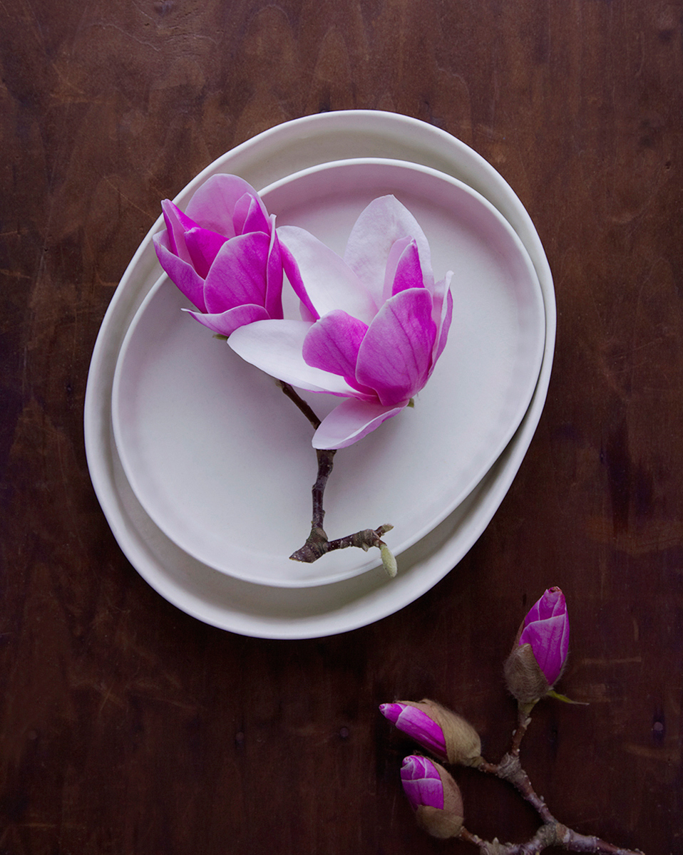 Pink flowers sit atop two nesting ceramic plates on a wooden tabletop