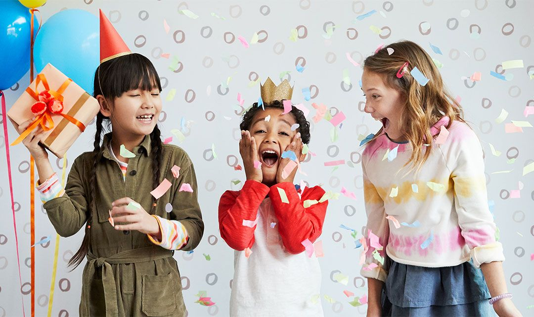 three kids in birthday hats laughing at a birthday party