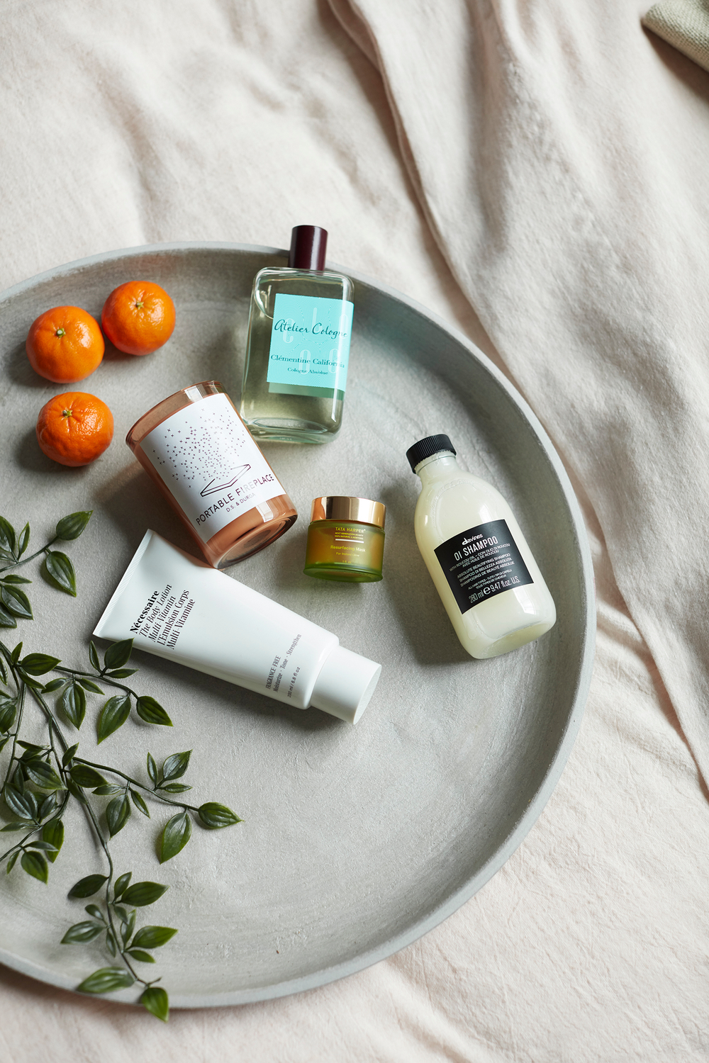 lotion, cream, cologne, portable fireplace, mandarins and green leaves. Using fruits and plants in product photography, linen sheets, gift display Beauty products for a self care day