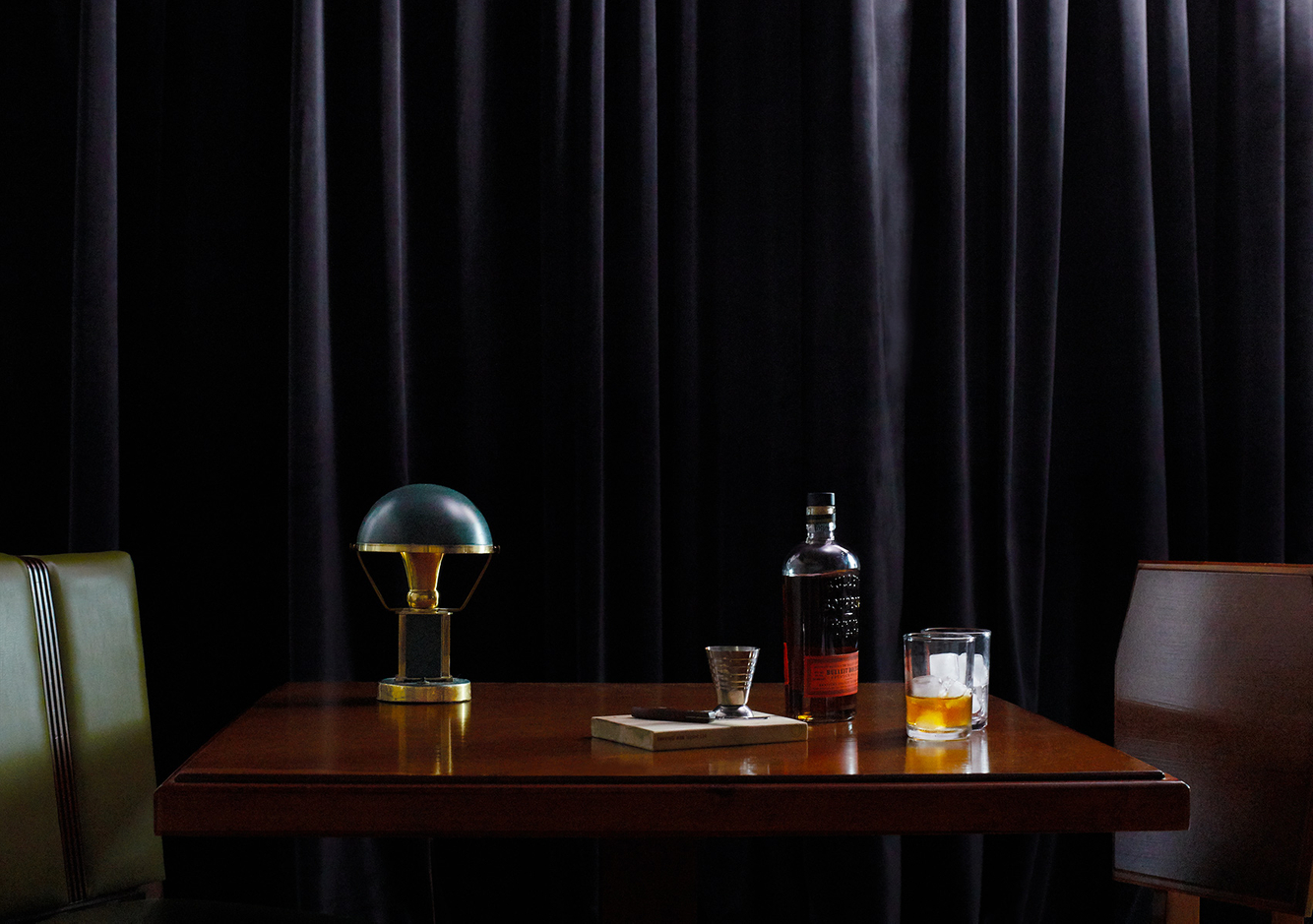 Green vintage desk lamp sits with liquor in a dark room 