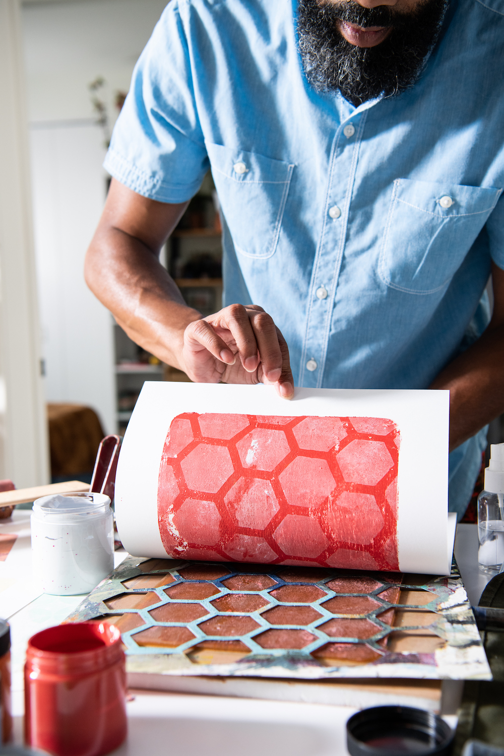 A man in a blue shirt carefully lifts paper to expose the way the ink has transferred Black artist at work