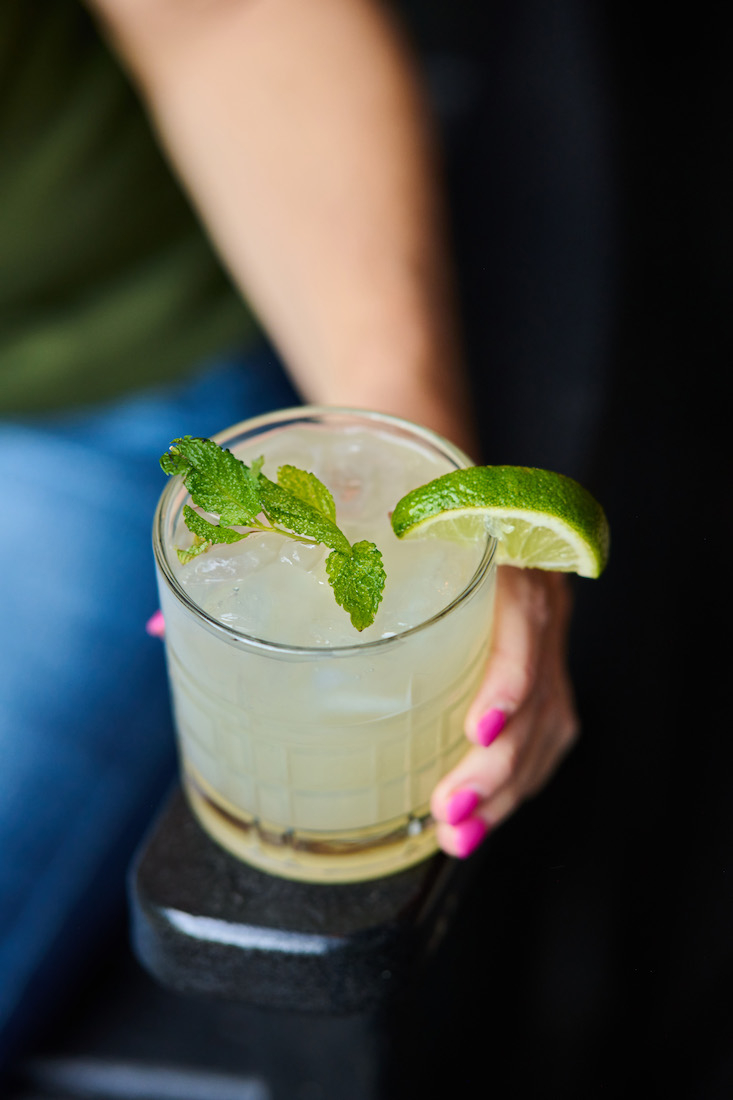woman with pink nails holds a minty mojito in glass 