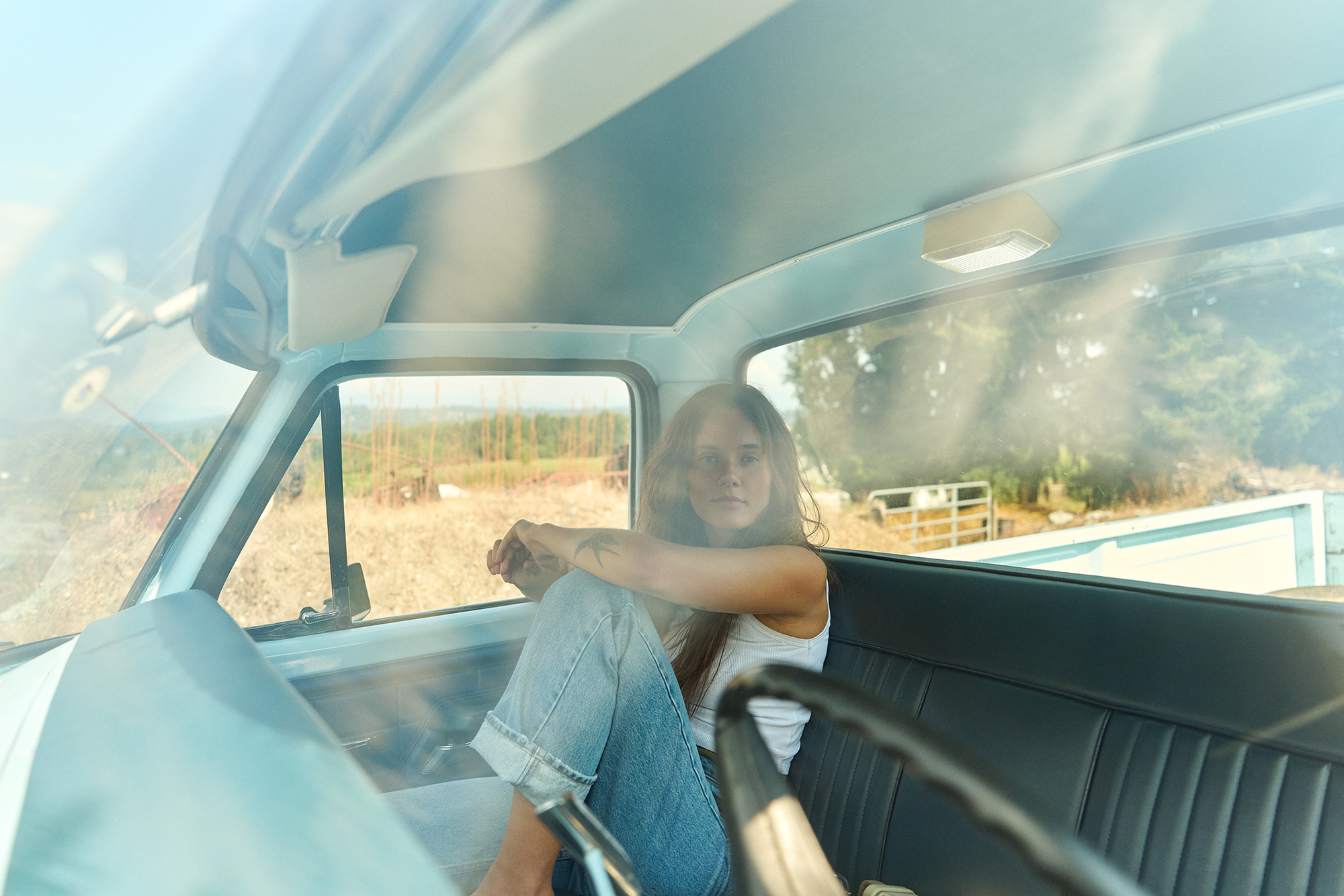 young woman sits in the passenger seat of vintage blue pick up truck 