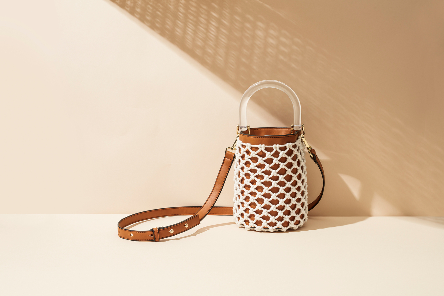 Luxury handbag shown in front of beige wall with beautiful shadows cast Lucite handle and leather bucket bag with netting