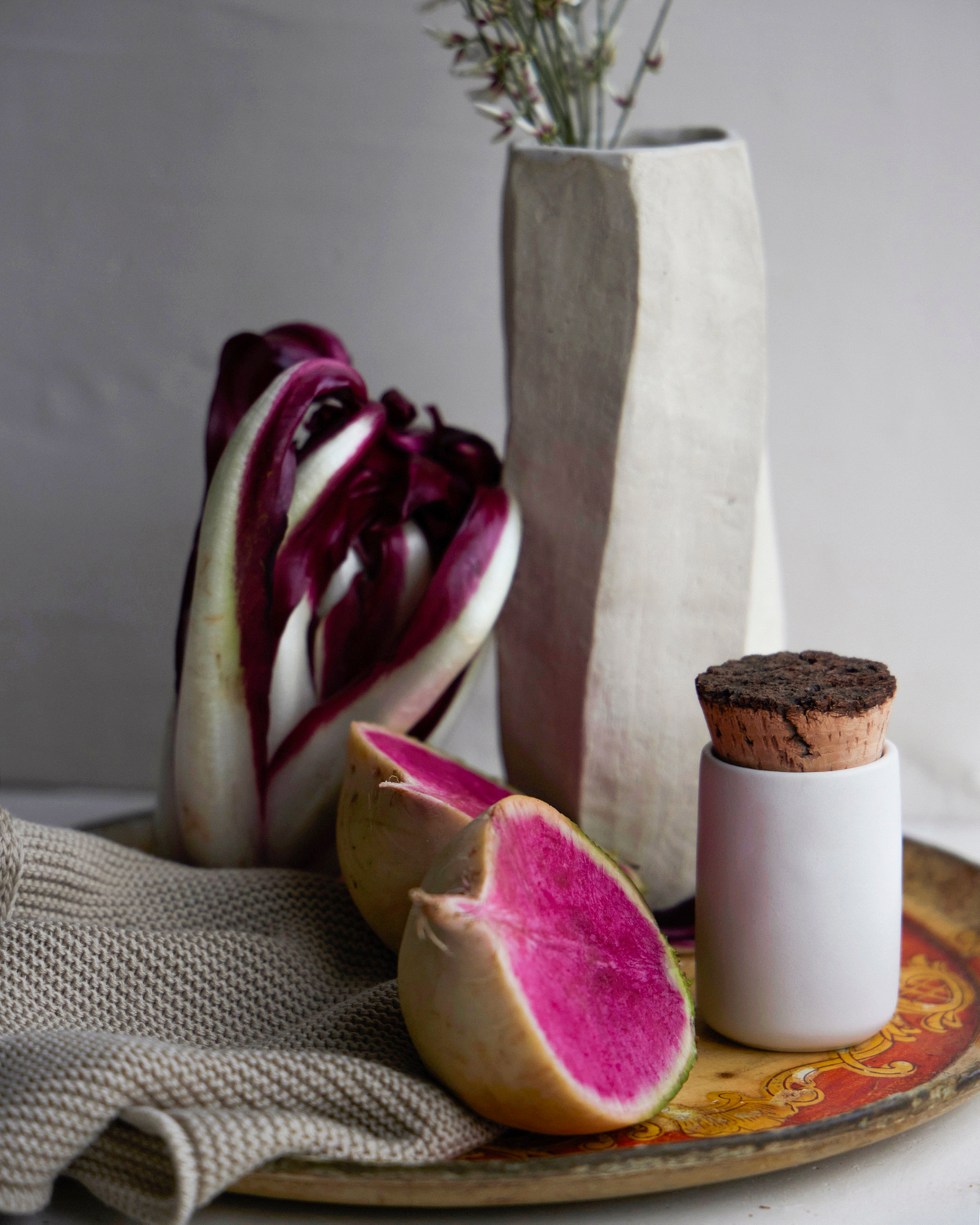 Sculptural vase sits on an antique circular food tray with to vegetables and a spice jar