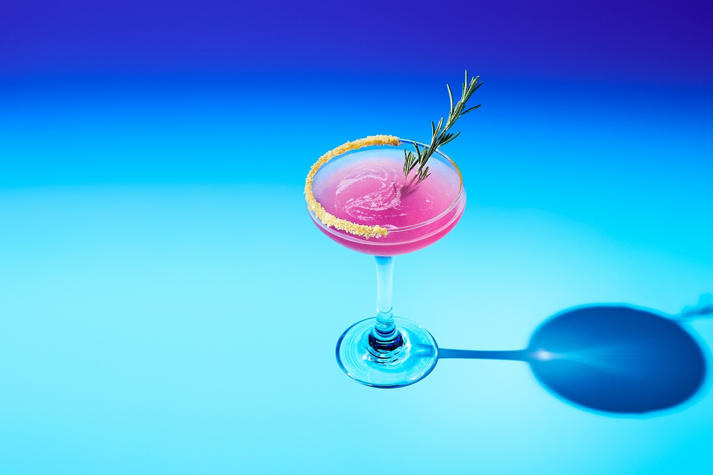 Pink cocktail in a martini glass on blue gradient