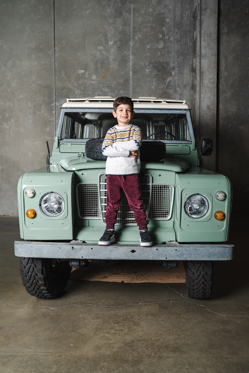 young boy stands on hood of green jeep 