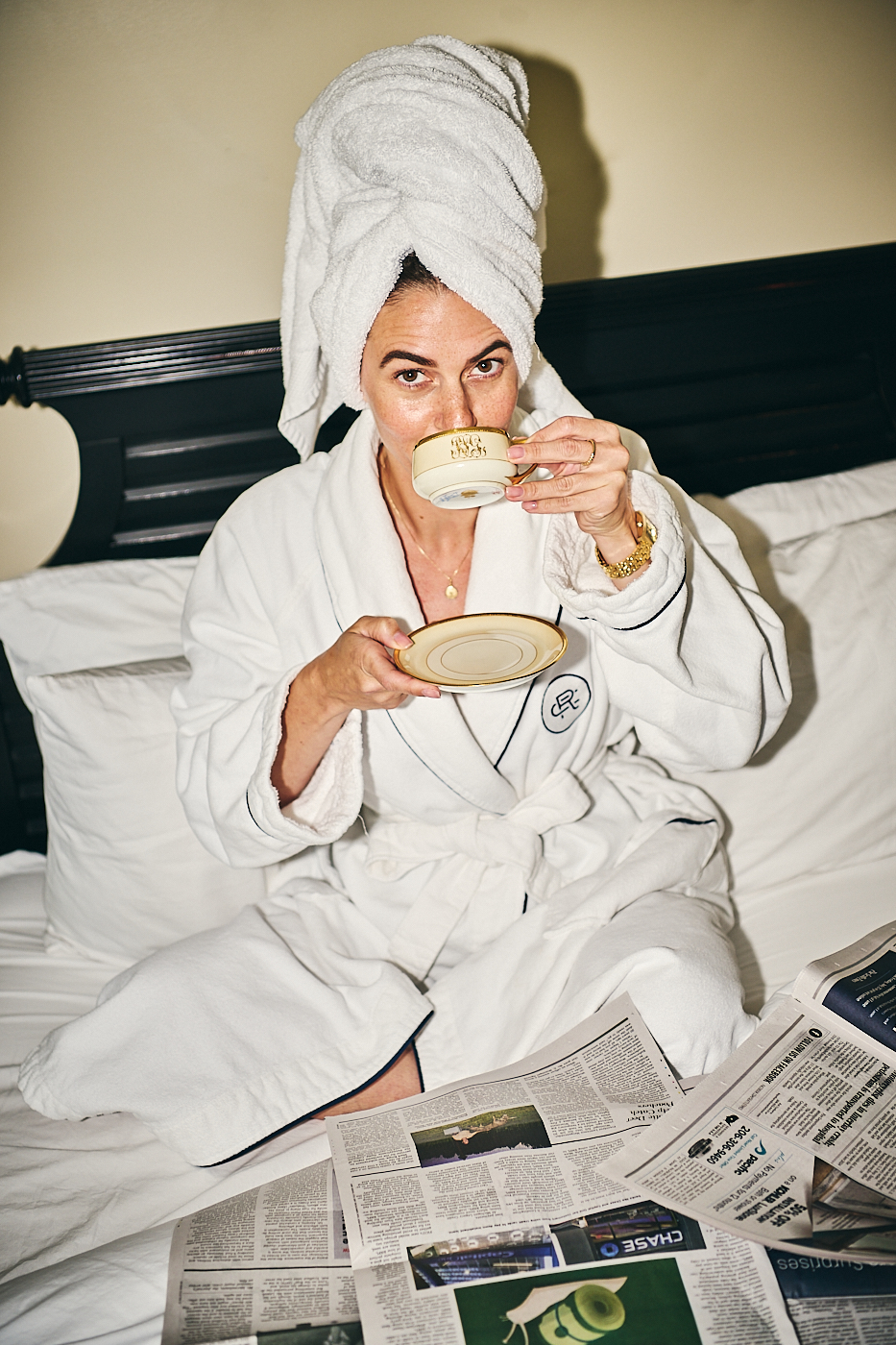 woman sips tea and reads newspaper in plush hotel bed 