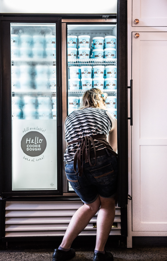 A service worker reaches into a freezer to organize artisanal ice cream products Facing products