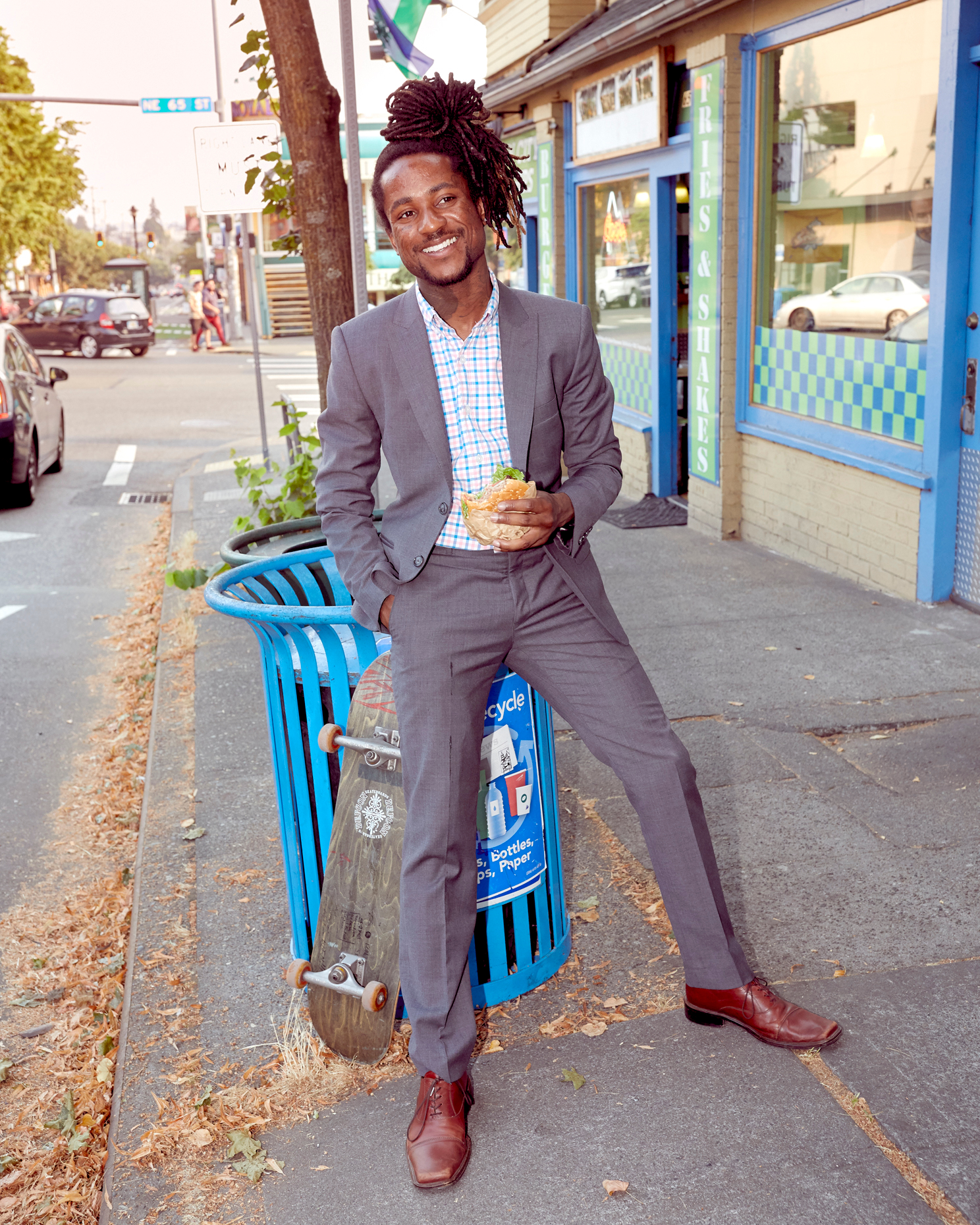 young black business man leans on trash can with skateboard 
