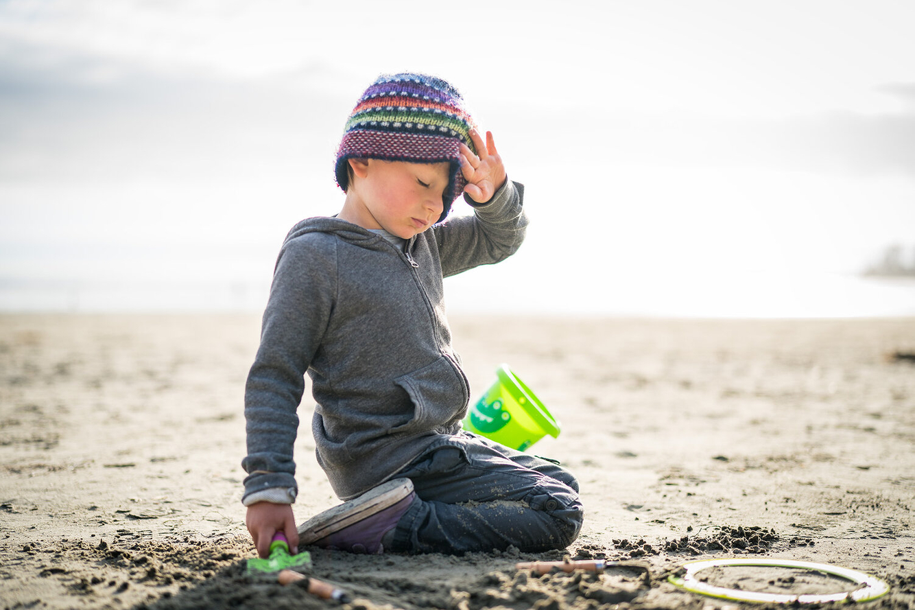 little boy in a beanie plays in the beach sand 