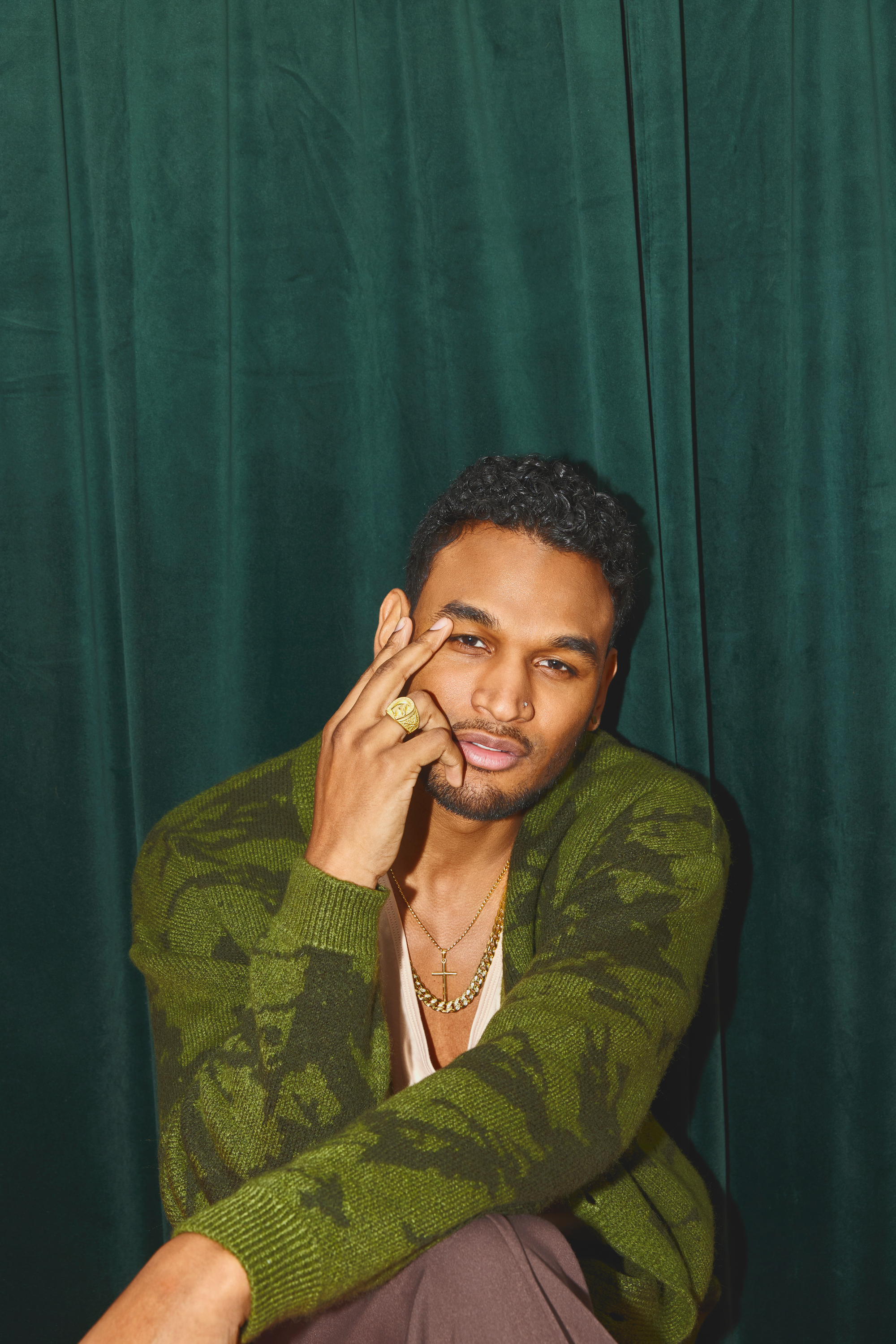 portrait of a cool edgy young black man in green camo cardigan 