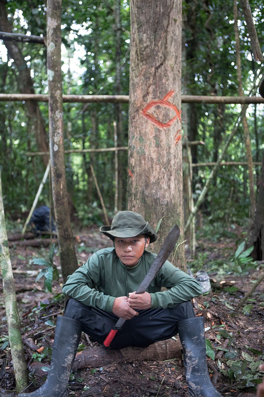 Young Korubo boy Seatvo (15) sits beneath a sign, made by a FUNAI team member, into a tree indicating the presense of 'friendly' people. Should uncontacted people enter the area in the future they would recognise this as non threatening.
Seatvo is listening to Expedition leader, Bruno Pereira (38), explaining the route and the security of the group during the expedition. The group were to walk in a particular order (armed members at the front and back) should they come across uncontacted people they were to stand still keep together and will try to communicate with the people. Amazon