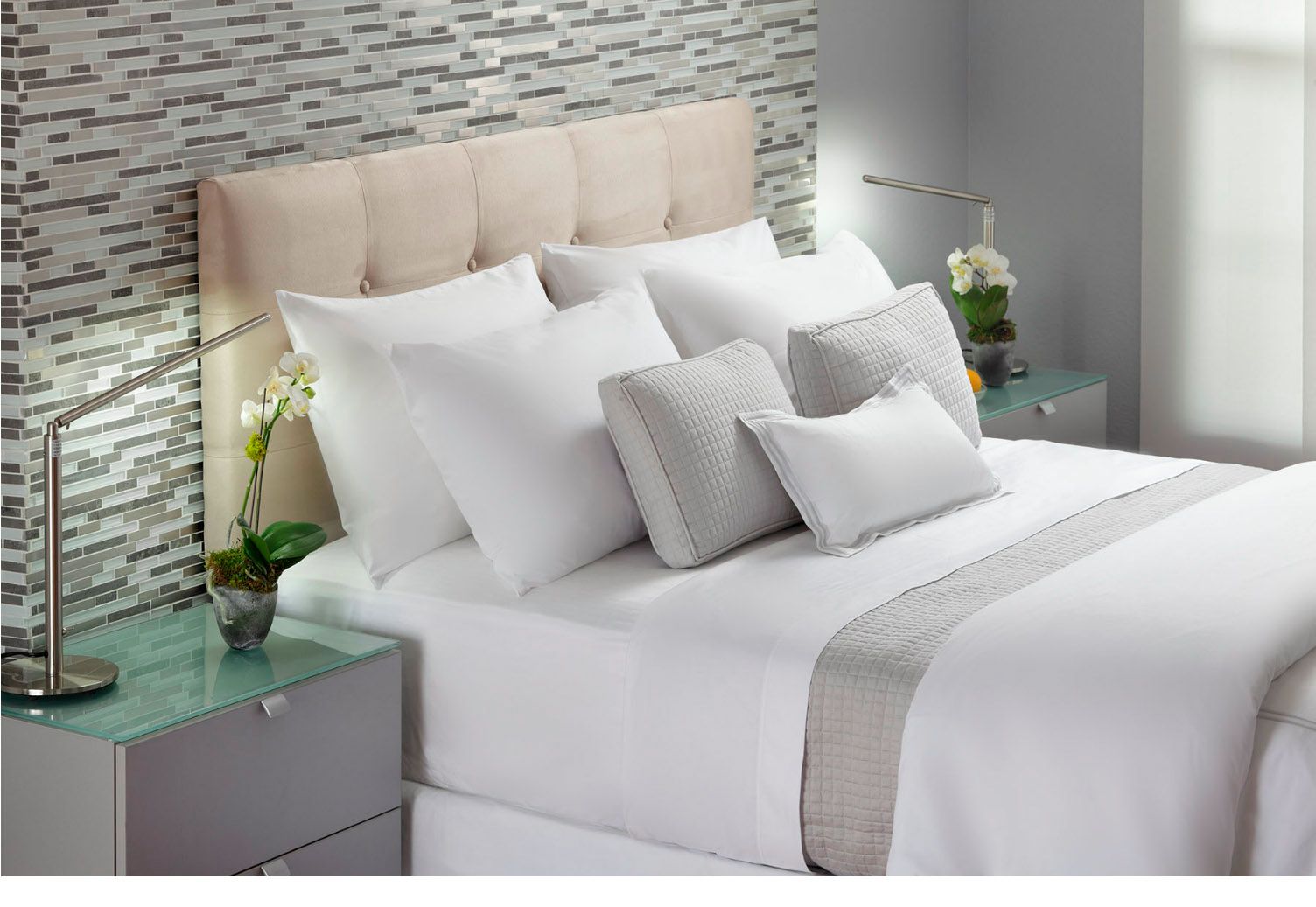 Interior design detail of a modern luxury bedroom with styled linens and a mosaic tile accent wall