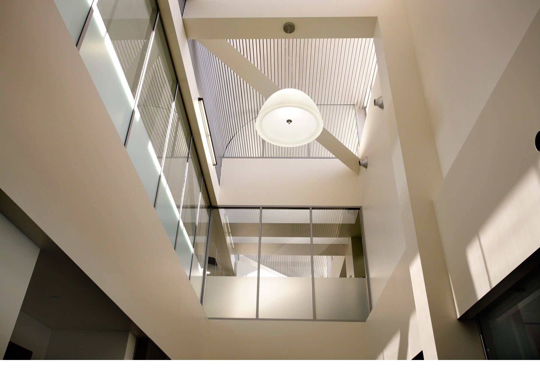 Architectural detail of a dome pendant light integrated with a structural crossmember beam in a modern interior atrium