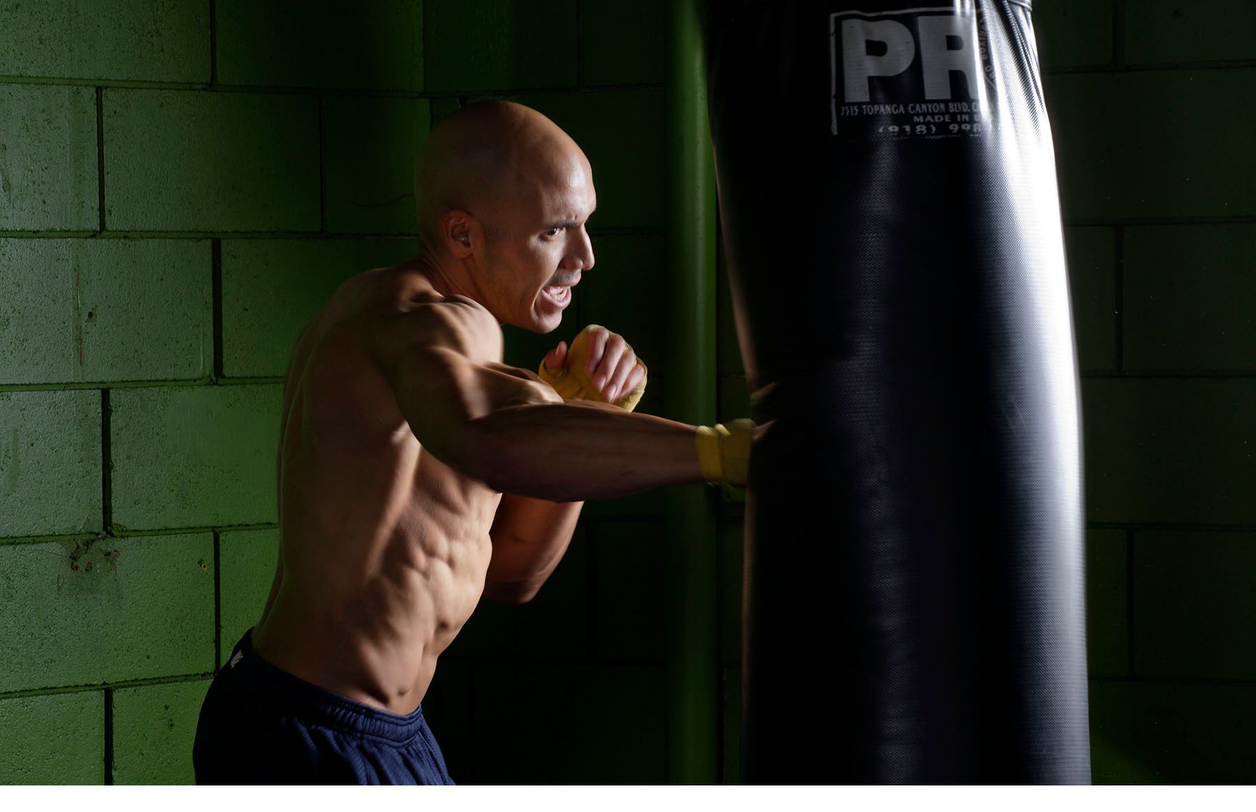 Male boxer striking heavy punching bag in gym